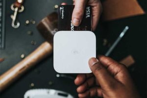 Close-up of a hand holding a credit card while using a small card reader device
